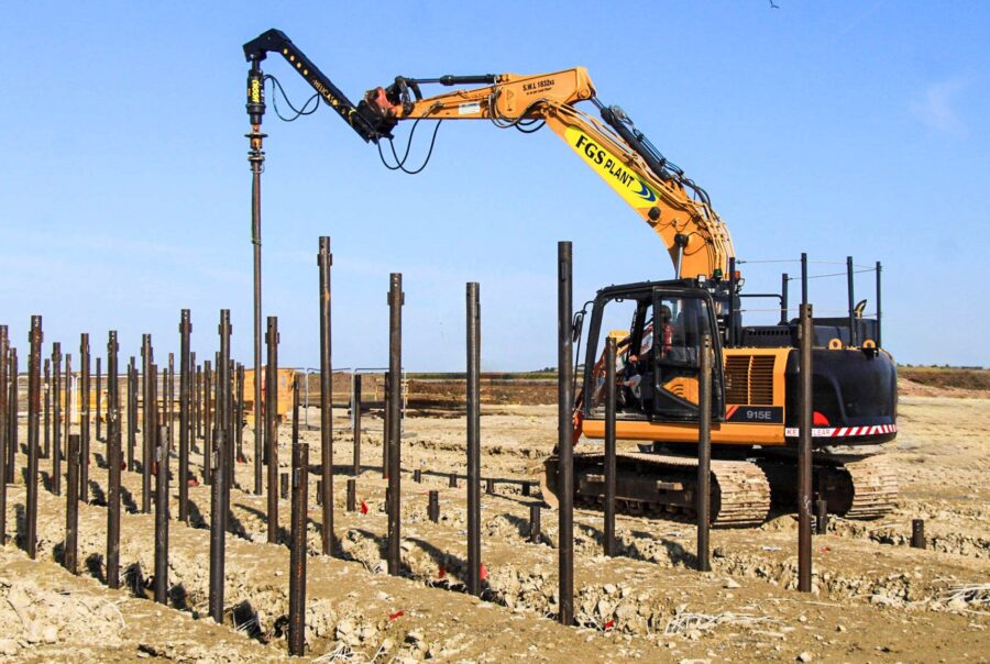 Excavator installing screw piles at solar project